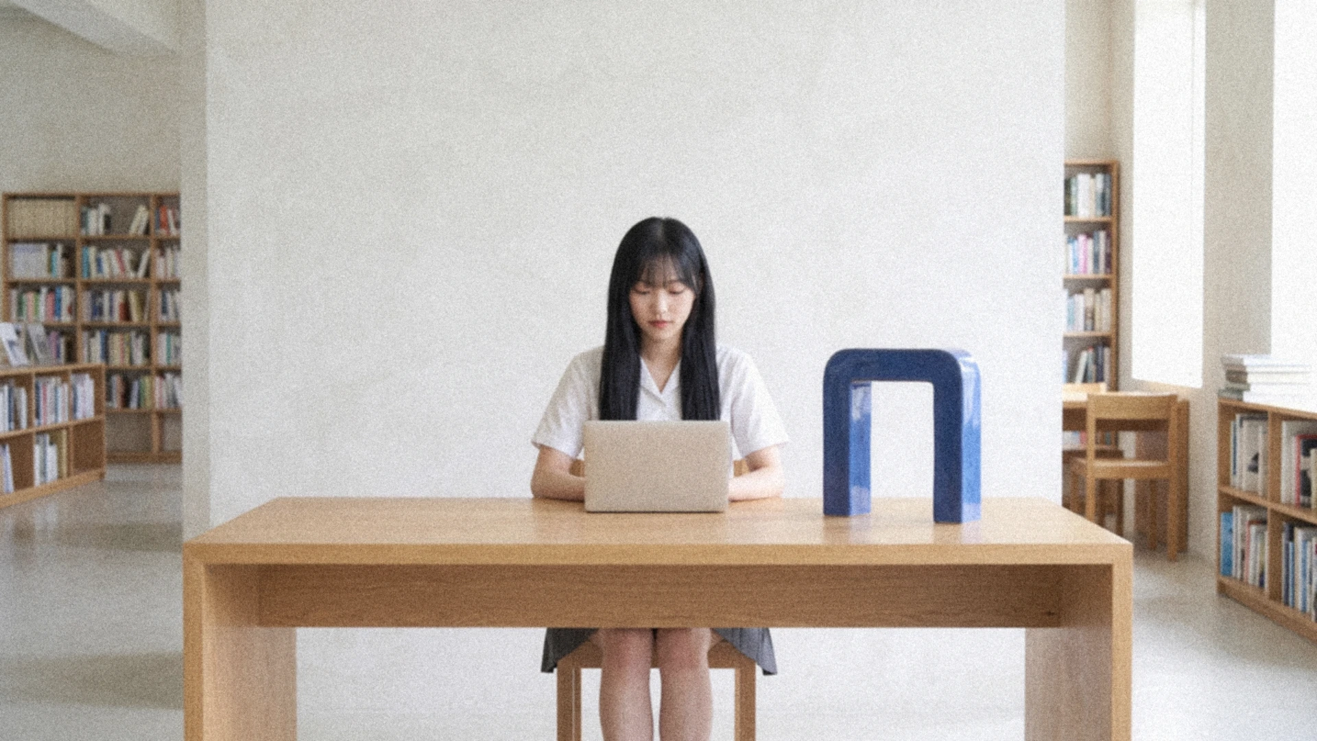 黑長髮的年輕女性在圖書館書桌前使用筆電,桌上放著鈷藍陶瓷拱門。